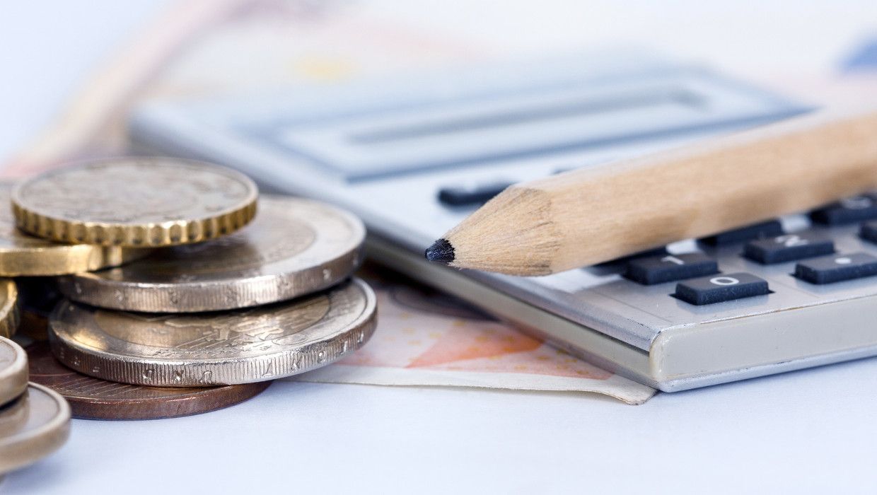 Kleingeld neben einem Taschenrechner, darauf ein Stift